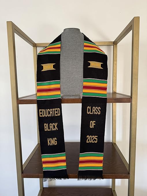 A custom black Kente stole displayed on a mannequin, adorned with vibrant red, yellow, and green stripes. The stole is embroidered with "EDUCATED BLACK KING" on the left panel and "CLASS OF 2025" on the right panel in gold lettering.