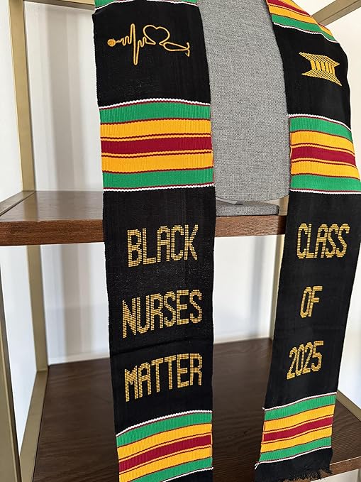 A custom Kente-style graduation stole displayed on a mannequin, featuring bold African-inspired colors. The stole is embroidered with "BLACK NURSES MATTER" and "CLASS OF 2025" in gold, alongside a stethoscope symbol and a traditional pillar motif.