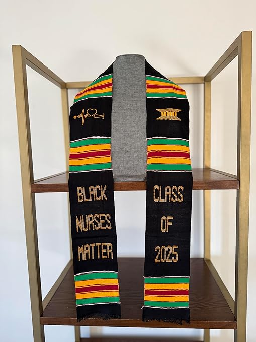 A beautifully woven black Kente stole with traditional African-inspired colors, celebrating Black nurses. The gold embroidery includes "BLACK NURSES MATTER" and "CLASS OF 2025," along with a stethoscope heartbeat symbol and a gold architectural pillar.