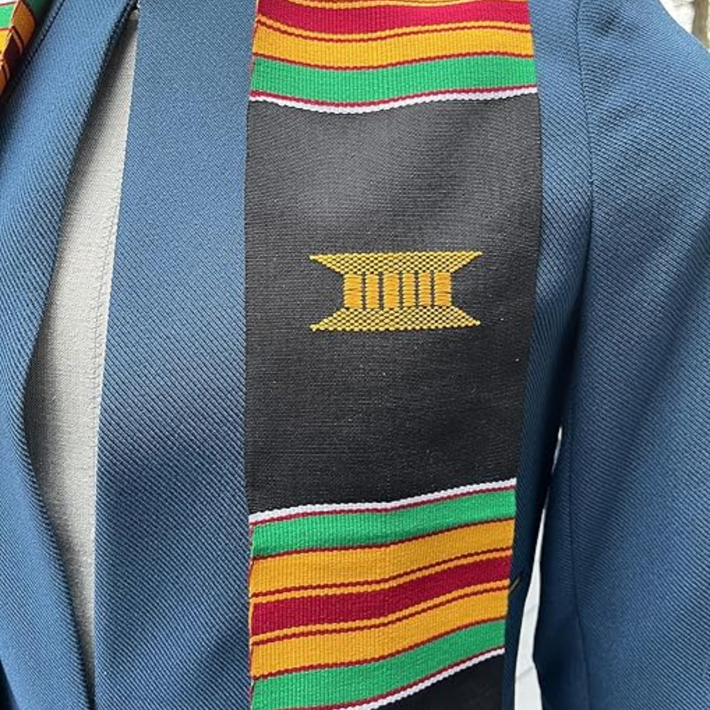 A close-up image of a black and yellow RN kente graduation stole featuring a custom kente pattern with alternating green, yellow, and red stripes. The photo is zoomed in to showcase the intricate details of the pattern.