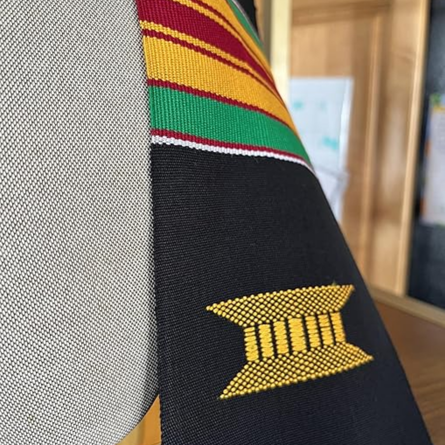 A close-up image of a black and yellow RN kente graduation stole featuring a custom kente pattern with alternating green, yellow, and red stripes. The photo is zoomed in to showcase the intricate details of the pattern.