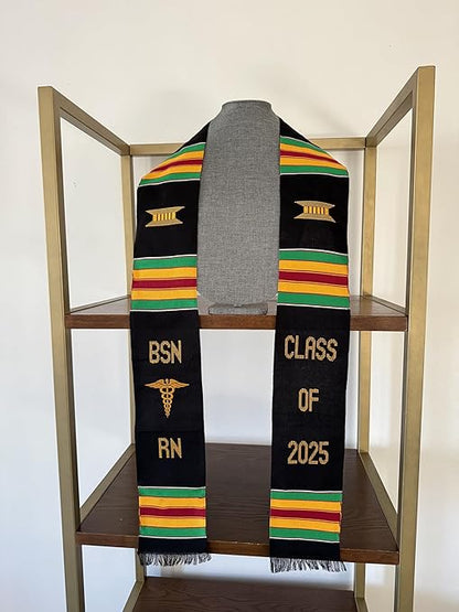 A black and yellow BSN RN Kente graduation stole featuring the bold vertical letters 'BSN RN' on the left, with a medical logo placed between 'BSN' and 'RN'. The phrase 'CLASS OF 2025' is embroidered horizontally on the right side of the stole. The stole showcases a custom Kente pattern with green, yellow, red, and green stripes, arranged in three sets on each side. The fabric is made of rayon.