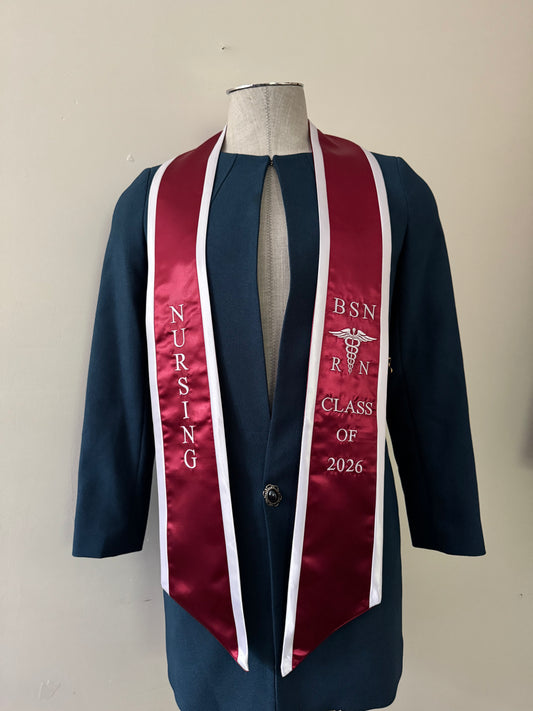 A burgundy with white trim BSN RN graduation stole, displaying bold 'BSN RN' lettering embroidered on the left, a medical logo with BSN RN on the right, and 'CLASS OF 2026' embroidered horizontally below. The stole has slanted tips and a white plain background. All text is embroidered.