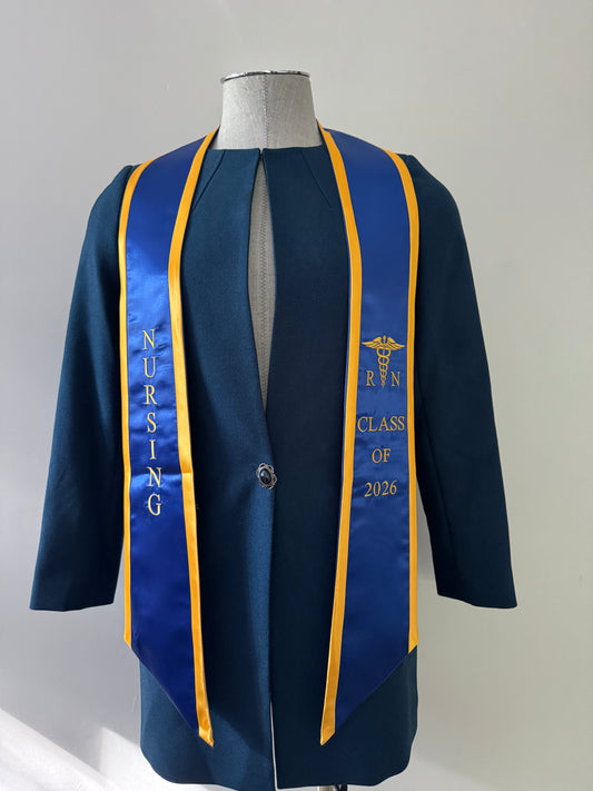 A Blue With Gold Trim RN Graduation Stole, displaying bold vertical 'NURSING' lettering on the right, a medical logo with 'RN' at the left, and 'CLASS OF 2026' embroidered horizontally below. The stole features slanted tips and a white plain background. All characters are embroidered.
