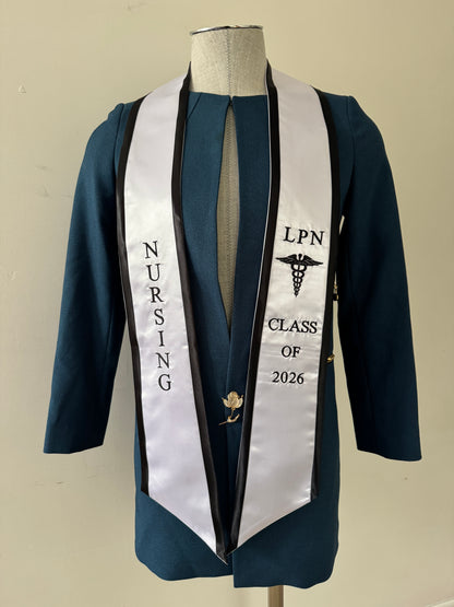A White With Black Trim LPN graduation stole with royal blue trim, showcasing bold 'LPN ' lettering embroidered at the top, followed by a medical logo and 'CLASS OF 2026' embroidered beneath. The stole has slanted tips and a white plain background. All characters are embroidered.