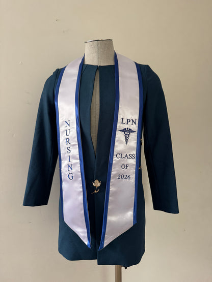 A White With Royal Blue Trim LPN graduation stole with royal blue trim, showcasing bold 'LPN ' lettering embroidered at the top, followed by a medical logo and 'CLASS OF 2026' embroidered beneath. The stole has slanted tips and a white plain background. All characters are embroidered.